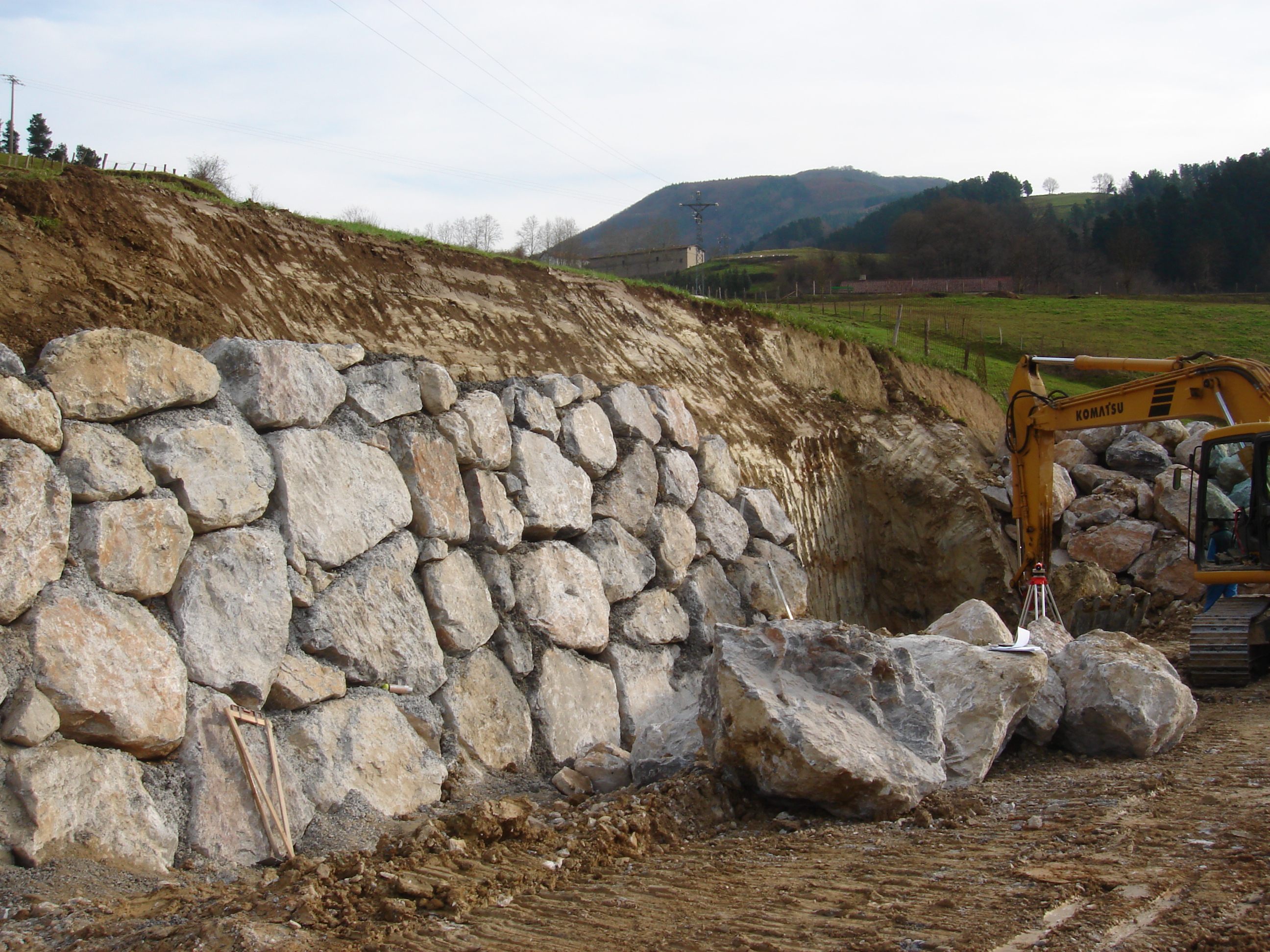 Large stone retaining wall under construction beside a sloped property